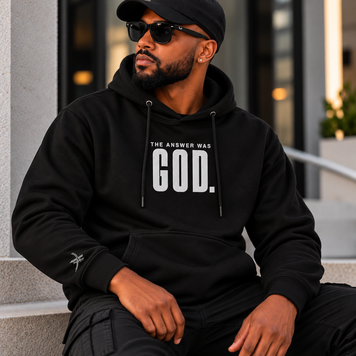 Man wearing a black hoodie with “THE ANSWER WAS GOD.” in white embroidery and a God Alone Apparel wrist logo.